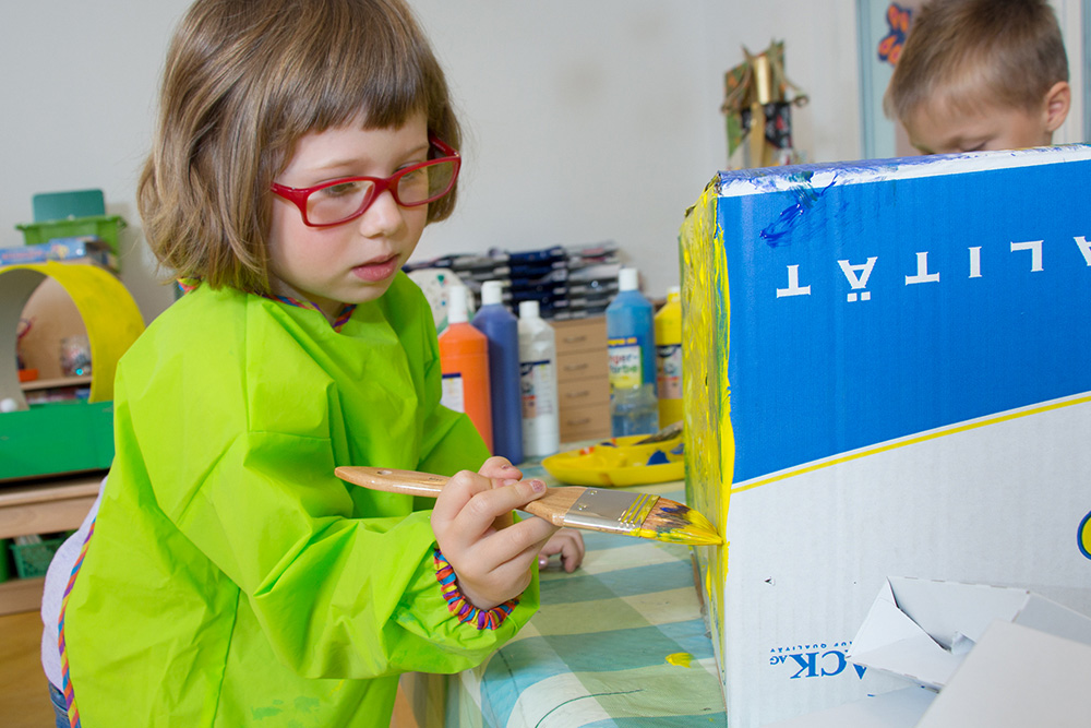 Mädchen malt einen Karton gelb an.