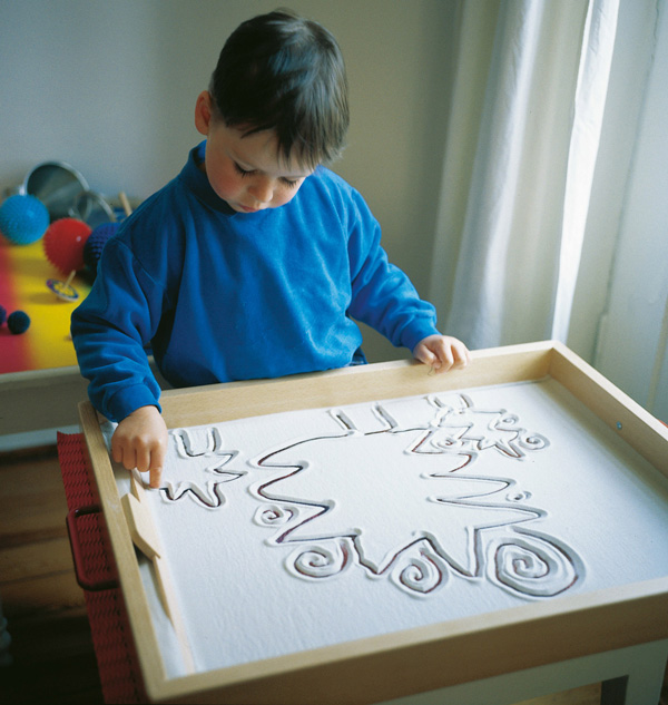 Kind zeichnet mit dem Finger in der Sandwanne